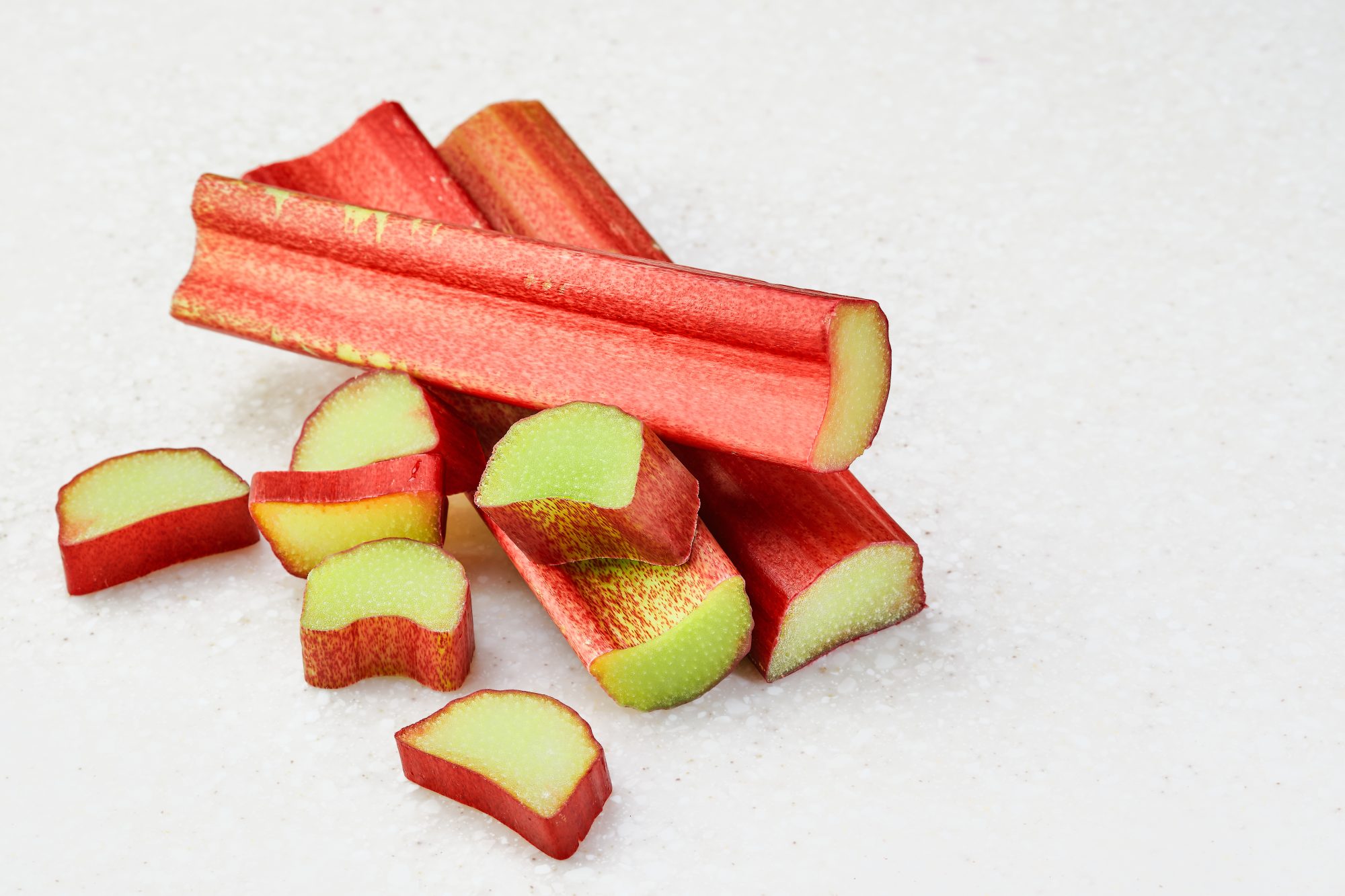 Elyxa Australian Organic Whole-food Supplements Sliced Stalk Of Rhubarb On A White Marble Background. Whole Rhubarb Sticks With A Few Pieces Of Chopped Rhubarb, Isolated, Ingredients For Making A Pie.